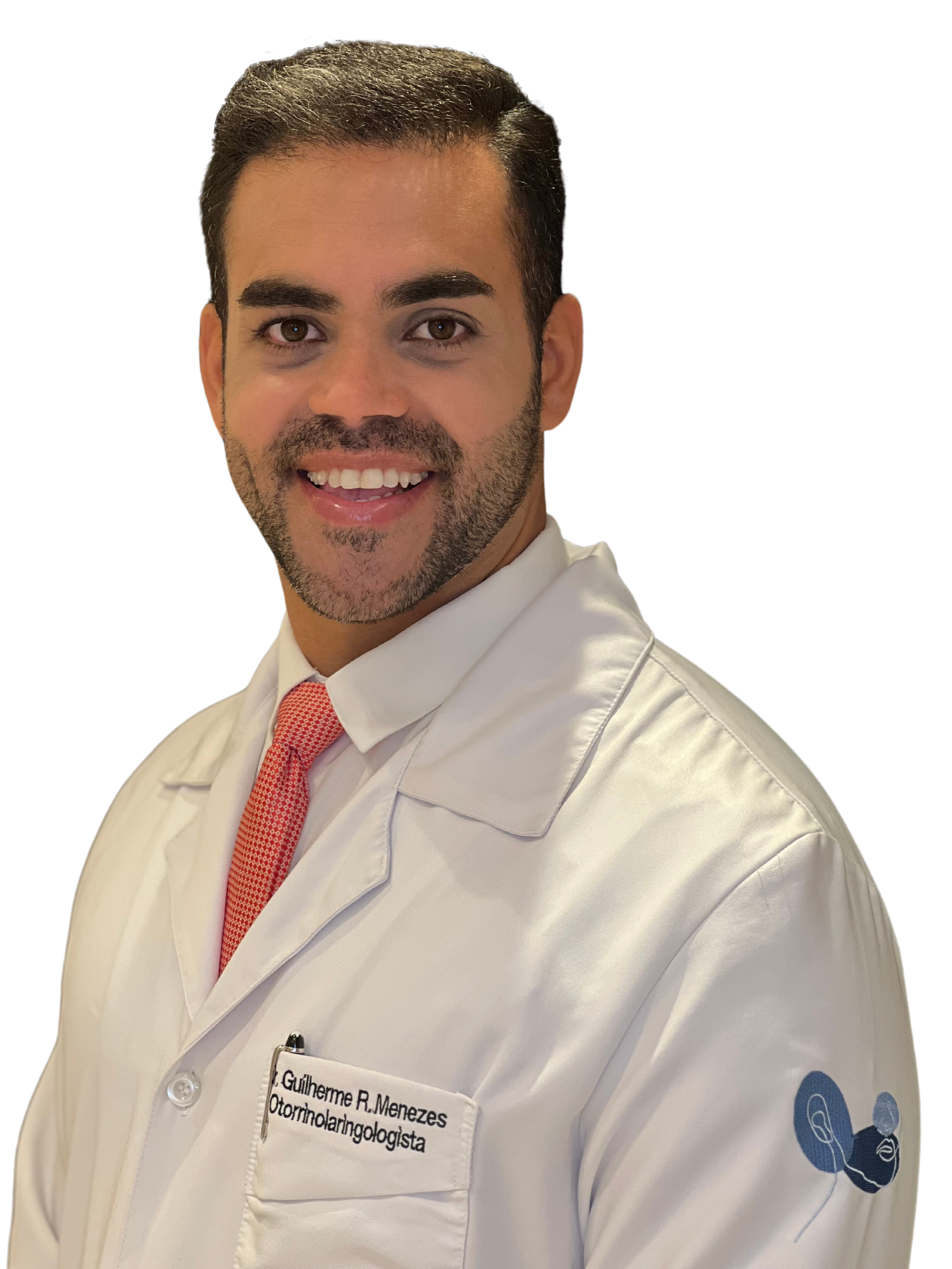 Dr Guilherme Menezes de jaleco e de perfil sorrindo