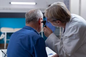 Médica usando instrumento de otologia para examinar infecção e dar aconselhamento médico ao homem idoso