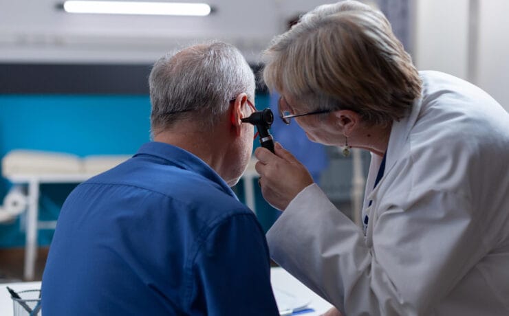 Médica usando instrumento de otologia para examinar infecção e dar aconselhamento médico ao homem idoso