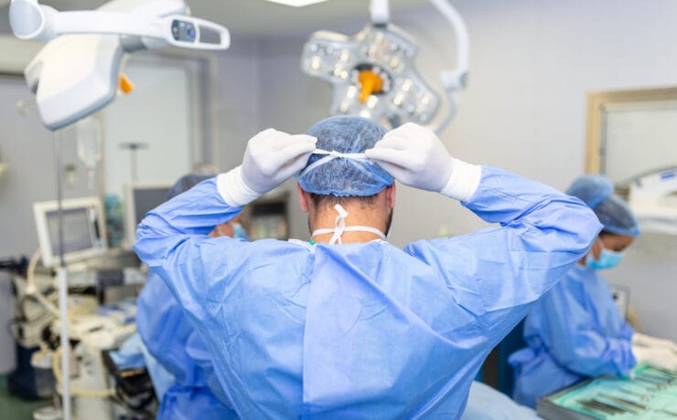 Vista traseira do cirurgião masculino usando máscara cirúrgica na sala de operações do hospital