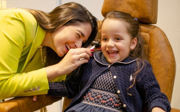 Dra Isabela Martins examinando sua paciente que sorri alegremente com a doutora.