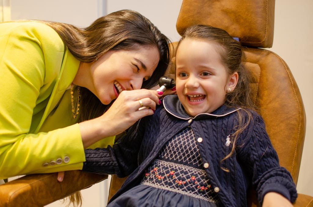 Dra Isabela Martins examinando sua paciente que sorri alegremente com a doutora.